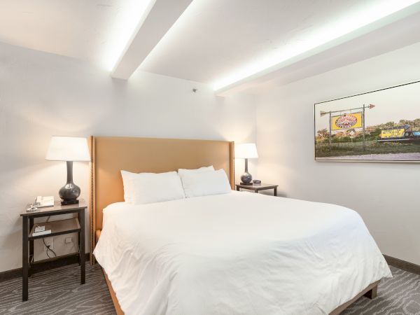 A hotel room with a large bed, white linens, two bedside tables with lamps, and a framed picture on the wall.