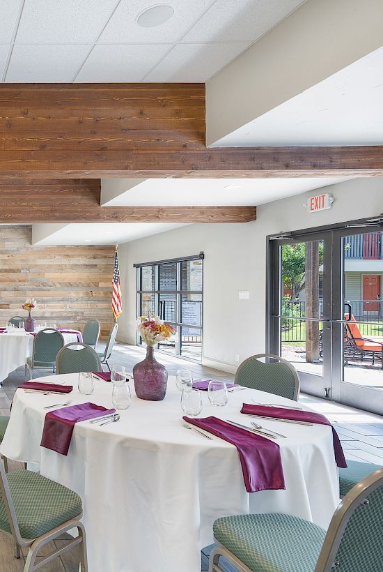 The image shows a modern event space with round tables, green chairs, and purple tablecloths, set up for a gathering with glass vases as decor.