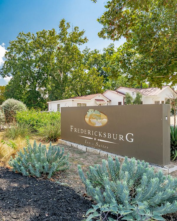 The image shows a landscaped area with a sign for Fredericksburg, featuring greenery and clear blue sky.