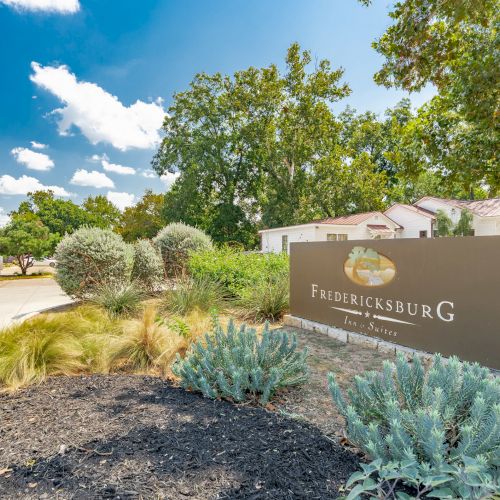 A landscaped area featuring a sign with "Fredericksburg" and a path lined with trees under a blue sky.