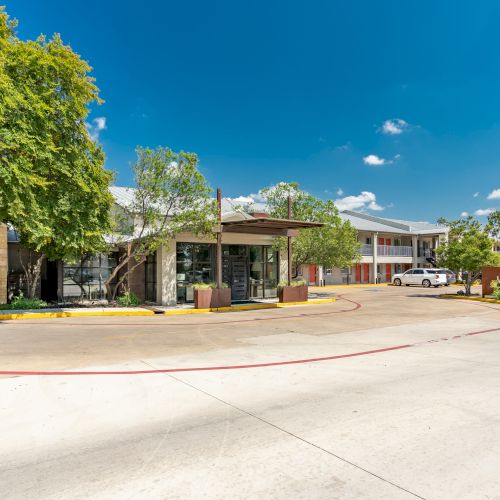 The image shows a building complex with trees, a driveway, and a clear sky.