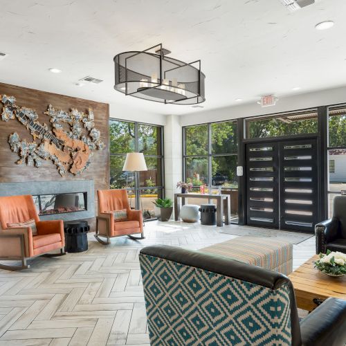 A modern lounge with natural light, cozy seating, decorative wall art, and a geometric floor pattern.