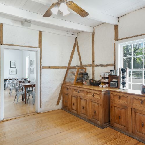 A kitchen with wooden cabinets, a coffee station, a window, and a view into a dining room.