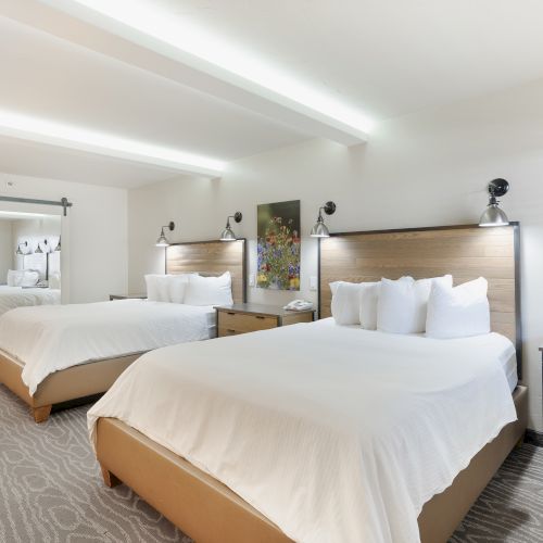 The image shows a hotel room with two double beds, a bathroom, and modern decor, creating a comfortable and inviting atmosphere for guests.