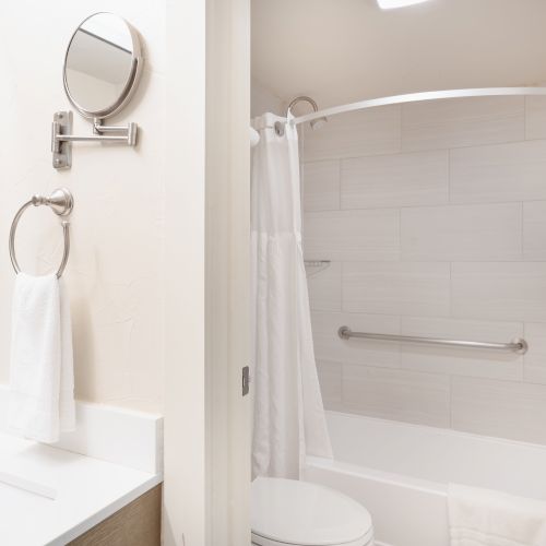 A modern bathroom with a sink, wall mirror, towel ring, and a bathtub with a shower curtain and grab bar.