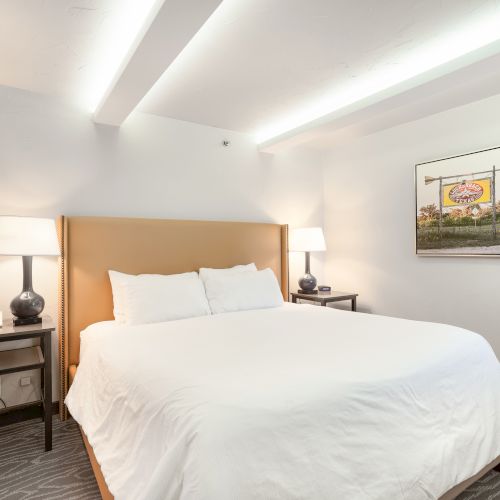 A neatly arranged hotel room with a large bed, two side tables with lamps, and a decorative picture on the wall.