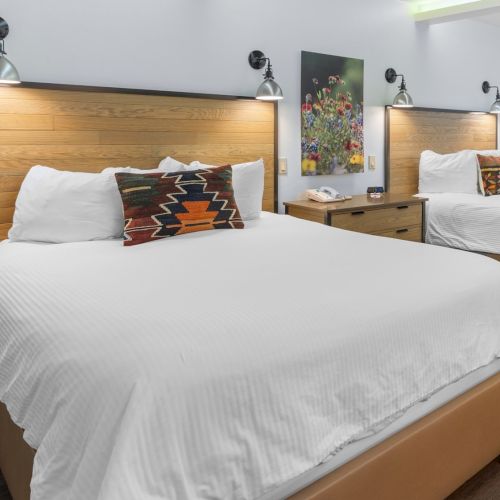 A modern hotel room with two twin beds, wooden headboards, floral wall art, and wall lamps.