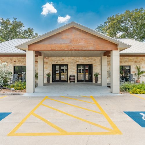 A small beige storefront-like building with a wooden awning, a couple of pillars, and a parking lot with blue handicap spaces in the foreground.