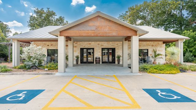 A wide-angle view of the hotel's exterior, showcasing its covered entrance, stone facade, and parking lot with handicap accessible parking spaces.