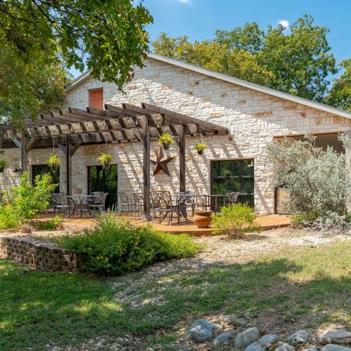 A single-story stone-and stucco house with a gable roof, lush lawn, and a short stone patio under a sunny, clear sky.