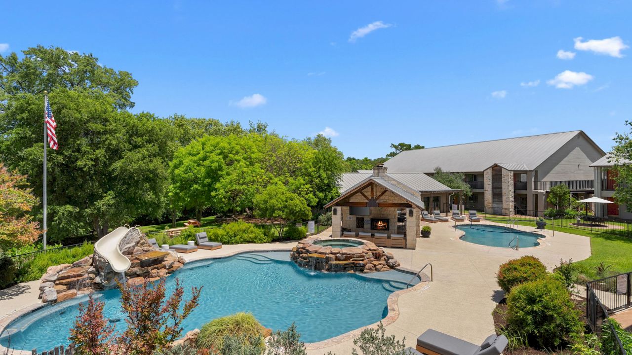 A large outdoor pool with a water slide and fire pit surrounded by trees and a building.